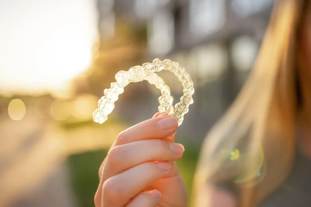 Person holding a clear Invisalign aligner tray up to the light outdoors