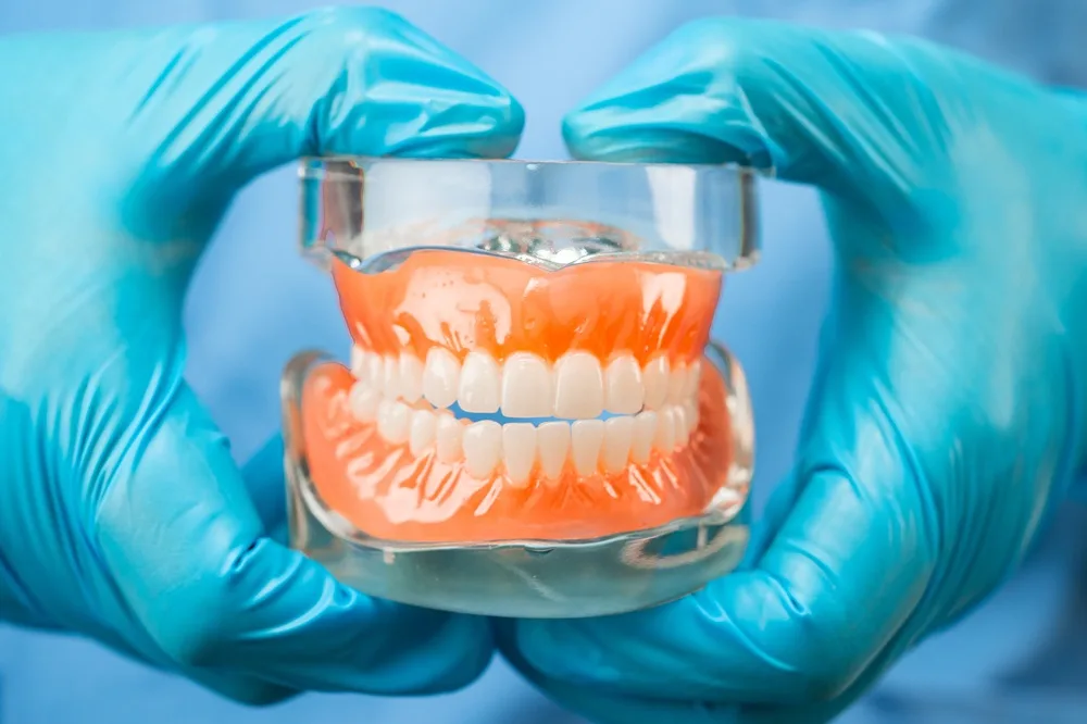 Blue-gloved hands holding a full denture model