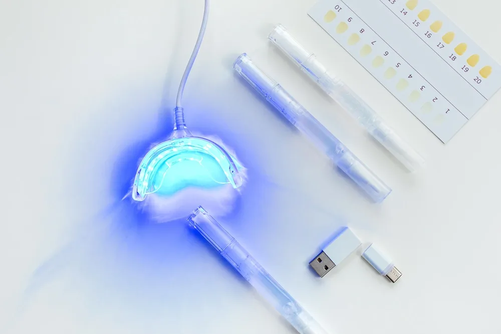Illuminated whitening tray, shade guide, and whitening pens on a white surface